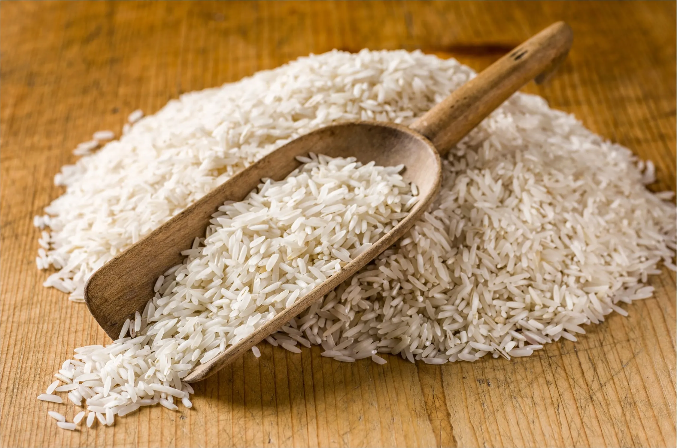Raw white rice heaped on a board with a wooden scoop